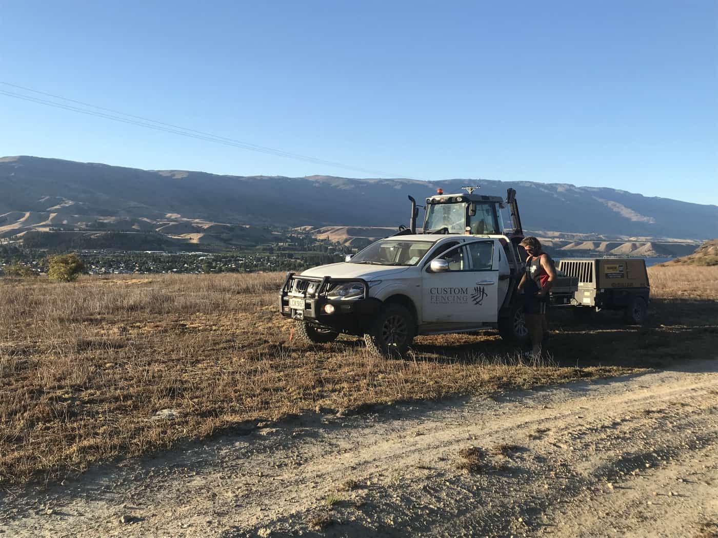 Fencing ute and wire trailer parked on a tussock ridge, with a wire fence line running away toward distant ranges