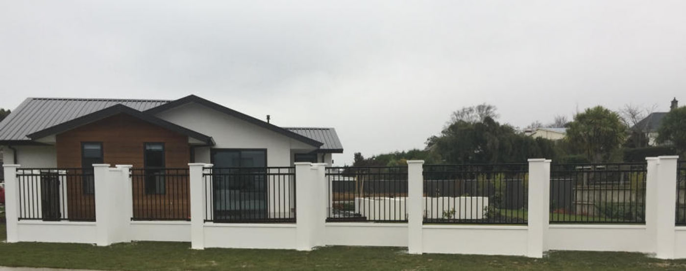 Black aluminium panel fence set into a rendered white plinth and piers along the street frontage of a modern single-storey house